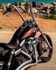 the motorcycle is parked on the side of the road near the water and rocks in the background