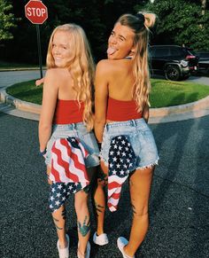 two young women standing next to each other in front of a stop sign with an american flag on it