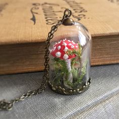 a small red mushroom in a glass dome with moss inside on a chain attached to a book