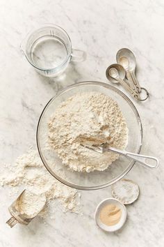 a bowl with some flour and measuring spoons next to it on a marble counter