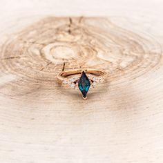 a blue diamond ring sitting on top of a piece of wood