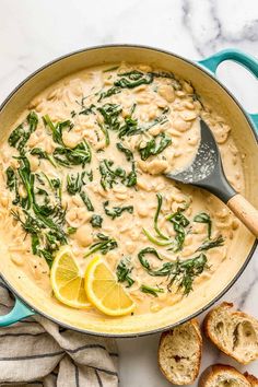 a large pot filled with pasta and spinach on top of a table next to bread