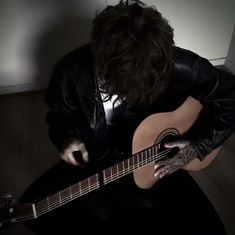 a man sitting on the floor playing an acoustic guitar