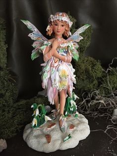 a figurine of a fairy with wings and flowers on her body standing on a rock