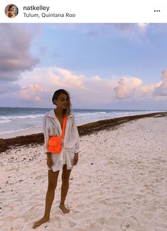 a woman standing on top of a sandy beach next to the ocean with an orange frisbee in her hand