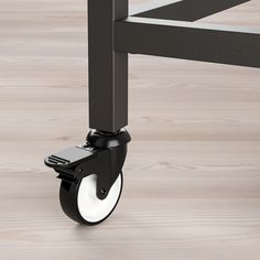 a close up of a black metal frame with wheels on a wood flooring area