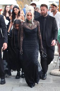 lady in black dress walking down the street with other people behind her wearing all black