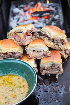 several sandwiches stacked on top of each other next to a bowl of soup in front of an open fire