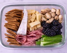 a glass container filled with meat, cheese and veggies next to crackers