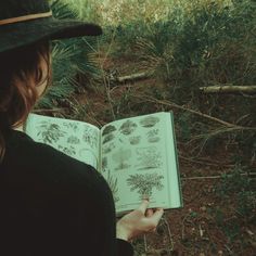 a woman is holding an open book in her hands and looking at the plants outside