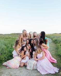 a group of women in dresses posing for a photo on a dirt path with tall grass