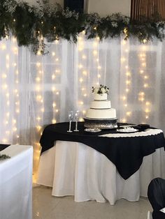 a table topped with a cake next to a window covered in fairy lights and greenery