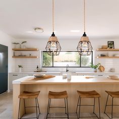 a kitchen island with four stools in front of it and two hanging lights above the island