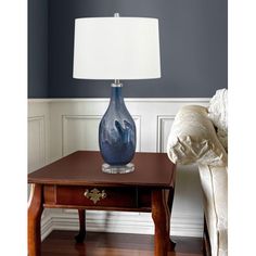 a blue vase sitting on top of a wooden table next to a white pillow and lamp