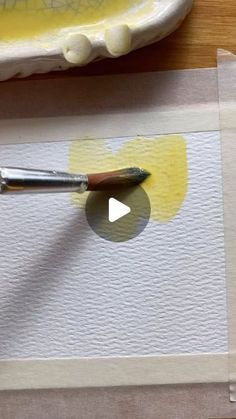 a person using a paintbrush to paint a piece of paper with yellow watercolors