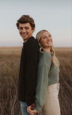 a young man and woman are standing in the middle of a field smiling at the camera