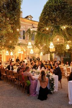 a group of people sitting at tables in front of some trees and buildings with lights on them