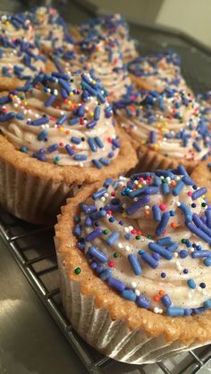 cupcakes with white frosting and sprinkles on a cooling rack