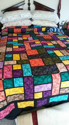 a bed with a multicolored quilt on it's headboard and foot board