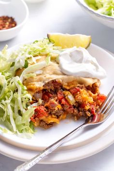 a white plate topped with tacos and salad next to a bowl of sour cream