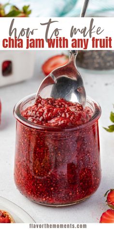 strawberry jam in a glass jar with a spoon and strawberries on the table next to it