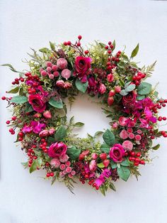 a wreath with red flowers and greenery on the outside of a white building wall