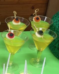 four glasses filled with yellow liquid and topped with olives, on a green tablecloth