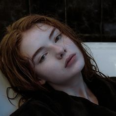 a woman with red hair laying down in a bathtub looking off into the distance