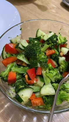 a glass bowl filled with vegetables on top of a wooden table