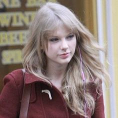 a woman with long blonde hair and headphones is looking at her cell phone while walking down the street