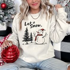 a woman sitting on a couch wearing a snowman sweatshirt and holding a christmas ornament