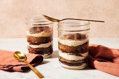 two jars filled with dessert sitting on top of a table next to a gold spoon