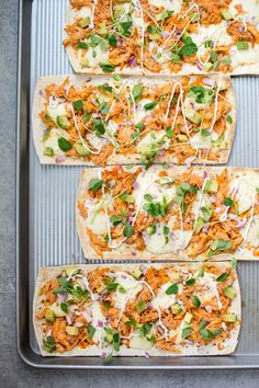 four flatbreads with shredded cheese and toppings on a baking sheet, ready to go into the oven