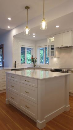 a large kitchen with white cabinets and wooden flooring, lights hanging from the ceiling