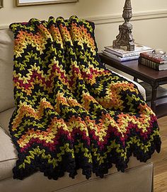 a crocheted blanket is sitting on a couch in front of a table and lamp