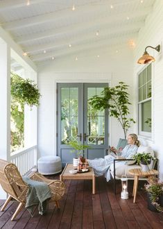 a woman sitting on a porch next to a potted plant and table with two chairs