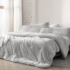 an unmade bed in a white room with brick walls and wooden flooring on the side