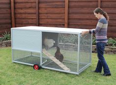 a woman standing next to a small cage with a cat in it on the grass