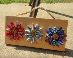 three colorful flowers are attached to a wooden sign