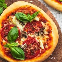 two small pizzas with basil, tomatoes and cheese on a cutting board next to each other