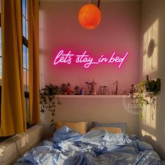 an unmade bed sitting under a neon sign