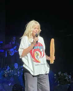 a woman holding a microphone in her right hand while standing next to a large piece of bread