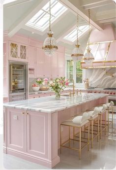 a large kitchen with pink cabinets and marble counter tops, gold chandeliers above the island