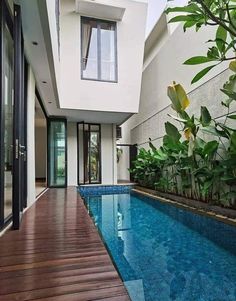 an empty swimming pool in front of a white house with wooden decking and glass doors