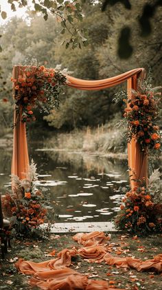 an outdoor wedding ceremony with orange draping and flowers on the water's edge