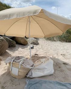 an open umbrella sitting on top of a sandy beach next to a bag and blanket