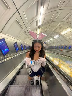 girl on escalator is white rabbit costume from Alice in wonderland. White corset, denim skirt, lace gloves, and white rabbit ears White Rabbit Costume Alice In Wonderland Party, Alice In Wonderland And White Rabbit, White Rabbit Alice In Wonderland Costume Women, Alice And Wonderland Bunny Costume, Alice And The Wonderland Costumes, Alice And Wonderland Rabbit Costume, The White Rabbit Halloween Costume, White Bunny Alice In Wonderland Costume, White Bunny Costume Alice In Wonderland