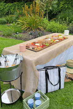 a picnic table with food and drinks on it in the middle of some grass area