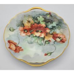 a plate with flowers painted on it and gold trimming around the edge, sitting on a white surface