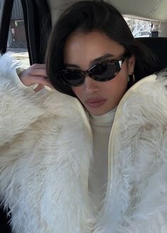 a woman sitting in the back seat of a car wearing sunglasses and a fur coat